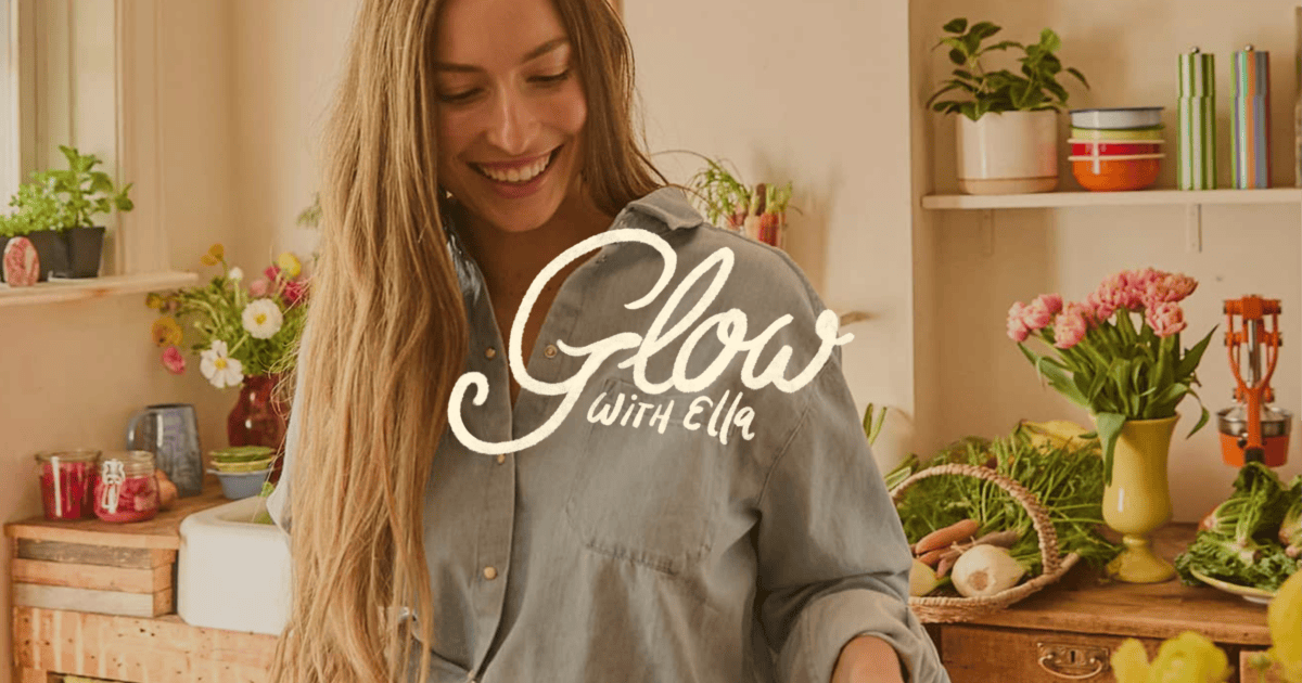 A woman in a kitchen smiles while preparing food, surrounded by fresh vegetables, flowers, and kitchenware. The text "Glow with Ella" appears over the image. | Wonderly