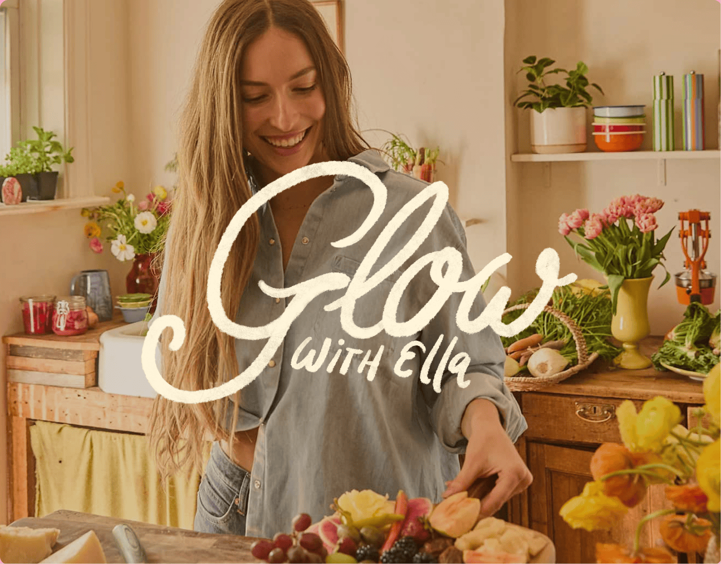 A woman stands in a bright kitchen preparing fruit, surrounded by flowers and kitchenware. Text on the image reads, "Glow with Ella. | Wonderly