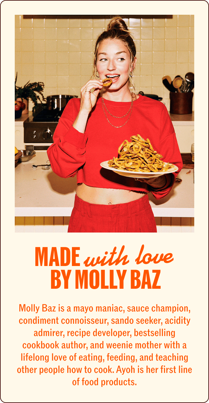A woman in a red outfit holds a plate of fries in one hand and eats a fry with the other hand, smiling in a kitchen setting with text about Molly Baz below. | Wonderly