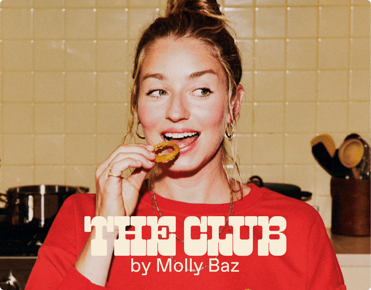 A woman in a red shirt eats a cookie in a kitchen, with the text "THE CLUB by Molly Baz" overlaid on the image. | Wonderly