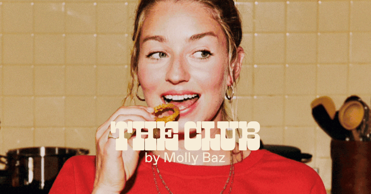 A woman in a red shirt eats food in a kitchen, with the text "THE CLUB by Molly Baz" overlaid on the image. | Wonderly