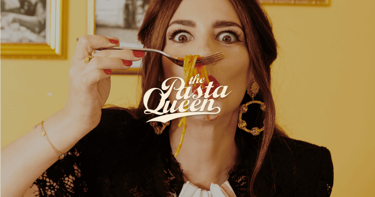A woman with wide eyes holds a forkful of pasta near her mouth. Text over the image reads “the Pasta Queen.”. | Wonderly
