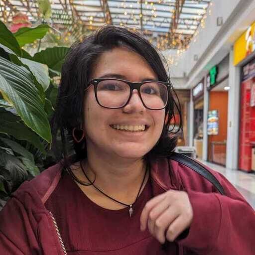 A person with glasses smiles in a shopping mall, with plants and shops visible in the background. | Wonderly