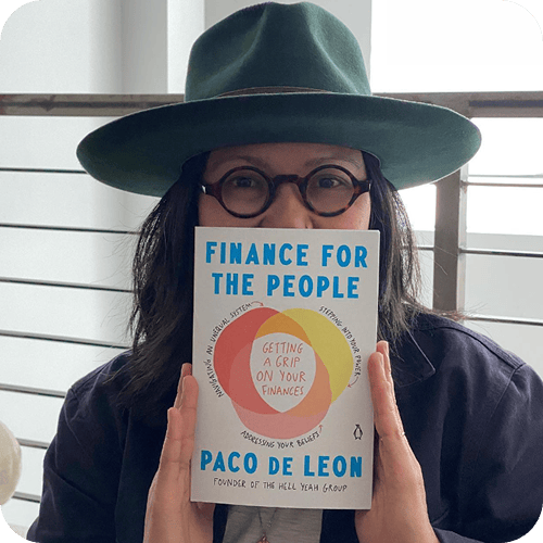 Person wearing a green hat and round glasses holds up the book "Finance for the People" by Paco de Leon, partially covering their face. | Wonderly